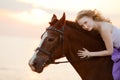 Beautiful woman riding a horse at sunset on the beach. Young girl with a horse in the rays of the sun by the sea. Royalty Free Stock Photo