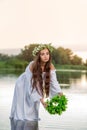 Beautiful woman on the river bank. Rustic woman with a wreath in a transparent dress