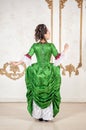Beautiful woman in rococo style medieval dress standing near wall back pose