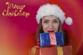 Beautiful woman in a santa claus hat, smiling and peeking out from behind the christmas presents Royalty Free Stock Photo