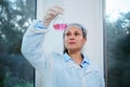 Beautiful woman scientist, medical biologist, pharmacologist in lab coat examines the fluid substance in glass flask Royalty Free Stock Photo