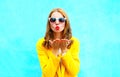 Beautiful woman sends an air kiss in yellow coat on colorful