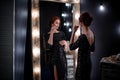 Beautiful woman in shiny black evening dress stands next to dark high mirror Royalty Free Stock Photo