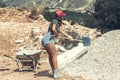 Beautiful woman in the shorts and in the red peaked cap with a wheelbarrow for cement and the shovel digging on stone. Concept