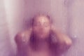 Beautiful woman in the shower behind glass with drops. Royalty Free Stock Photo