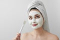 A beautiful woman after a shower at home with a towel on her head and with a cosmetic mask on her face with a brush in Royalty Free Stock Photo