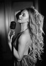 Beautiful woman sings into a microphone. Singer performs the song on dark stage Royalty Free Stock Photo