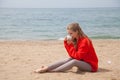 Beautiful blonde woman sits on the sand on an empty beach by the sea Royalty Free Stock Photo