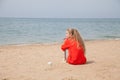 Beautiful blonde woman sits on the sand on an empty beach by the sea Royalty Free Stock Photo