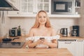 Beautiful woman sits at a table on the background of the kitchen at home. Girl with a smart smart phone in her hands. The blonde