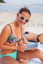 Beautiful woman sitting on the beach and using her tablet