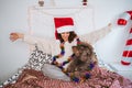 A beautiful woman sitting on the bed with her dog and looking at the pet with excitement at Christmas day. They are wearing