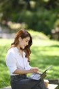 Woman sitting on bench in the city park and working with computer tablet. Royalty Free Stock Photo