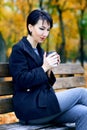 Beautiful woman sitting with coffee and dreaming in autumn city park, fall season, yellow leaves Royalty Free Stock Photo