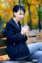 Beautiful woman sitting with coffee and dreaming in autumn city park, fall season, yellow leaves Royalty Free Stock Photo