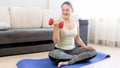 Beautiful young woman sitting on floor at living room and exercising with dumbbells Royalty Free Stock Photo