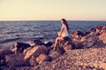 Beautiful woman sitting on the rock near the blue sea and sky wi Royalty Free Stock Photo