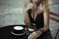 Beautiful woman sitting in the summer cafe holding her hand under the chin. Cup of tasty frothy latte and berry dessert in glass