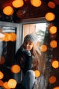 Beautiful woman sitting in a sweater home by the window. Blurred winter snow tree background. Morning, coziness, winter and people Royalty Free Stock Photo