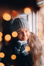 Beautiful woman sitting in a sweater home by the window. Blurred winter snow tree background. Morning, coziness, winter and people Royalty Free Stock Photo