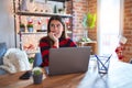 Beautiful woman sitting at the table working with laptop at home around christmas lights looking stressed and nervous with hands