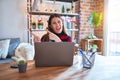 Beautiful woman sitting at the table working with laptop at home around christmas lights smiling and looking at the camera Royalty Free Stock Photo