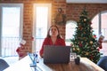 Beautiful woman sitting at the table working with laptop at home around christmas tree looking at the camera blowing a kiss on air Royalty Free Stock Photo