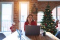 Beautiful woman sitting at the table working with laptop at home around christmas tree looking at the camera blowing a kiss with Royalty Free Stock Photo