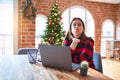 Beautiful woman sitting at the table working with laptop at home around christmas tree looking at the camera blowing a kiss with Royalty Free Stock Photo