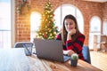 Beautiful woman sitting at the table working with laptop at home around christmas tree looking confident at the camera with smile Royalty Free Stock Photo