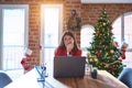 Beautiful woman sitting at the table working with laptop at home around christmas tree looking stressed and nervous with hands on