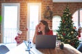 Beautiful woman sitting at the table working with laptop at home around christmas tree shouting and screaming loud to side with Royalty Free Stock Photo