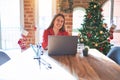 Beautiful woman sitting at the table working with laptop at home around christmas tree winking looking at the camera with sexy Royalty Free Stock Photo