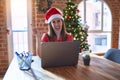 Beautiful woman sitting at the table working with laptop wearing santa claus hat at christmas with a big smile on face, pointing Royalty Free Stock Photo