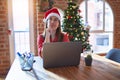 Beautiful woman sitting at the table working with laptop wearing santa claus hat at christmas with hand on chin thinking about Royalty Free Stock Photo