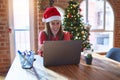 Beautiful woman sitting at the table working with laptop wearing santa claus hat at christmas with a happy and cool smile on face Royalty Free Stock Photo