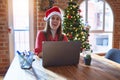 Beautiful woman sitting at the table working with laptop wearing santa claus hat at christmas happy face smiling with crossed arms Royalty Free Stock Photo