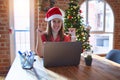 Beautiful woman sitting at the table working with laptop wearing santa claus hat at christmas looking confident with smile on Royalty Free Stock Photo