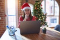 Beautiful woman sitting at the table working with laptop wearing santa claus hat at christmas looking stressed and nervous with Royalty Free Stock Photo