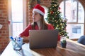 Beautiful woman sitting at the table working with laptop wearing santa claus hat at christmas looking to side, relax profile pose Royalty Free Stock Photo