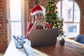 Beautiful woman sitting at the table working with laptop wearing santa claus hat at christmas shocked covering mouth with hands Royalty Free Stock Photo