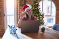 Beautiful woman sitting at the table working with laptop wearing santa claus hat at christmas smiling with happy face winking at Royalty Free Stock Photo