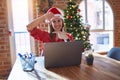 Beautiful woman sitting at the table working with laptop wearing santa claus hat at christmas smiling making frame with hands and Royalty Free Stock Photo