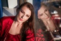 Beautiful woman sitting at the window in a red negligee, brooding view Royalty Free Stock Photo