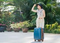 Beautiful Woman with a smile in a hat with a large suitcase on a background of palm leaves awaiting transfer.