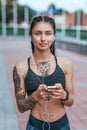 Beautiful woman smiling, happy girl in summer in city, tanned skin tattoo. Sportswear top. Phone earphones. Concept of Royalty Free Stock Photo