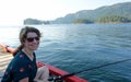 A beautiful woman smiling and happy sitting on a dock fishing with the ocean and forest in the background Royalty Free Stock Photo