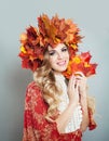 Beautiful woman smiling and holding fall leaves in hands. Pretty model with makeup, curly hair, autumn leaves crown