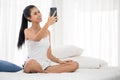 Beautiful woman smiling at a smartphone whlie sitting on the bed