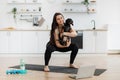 Woman holding Dachshund while squatting on mat at home